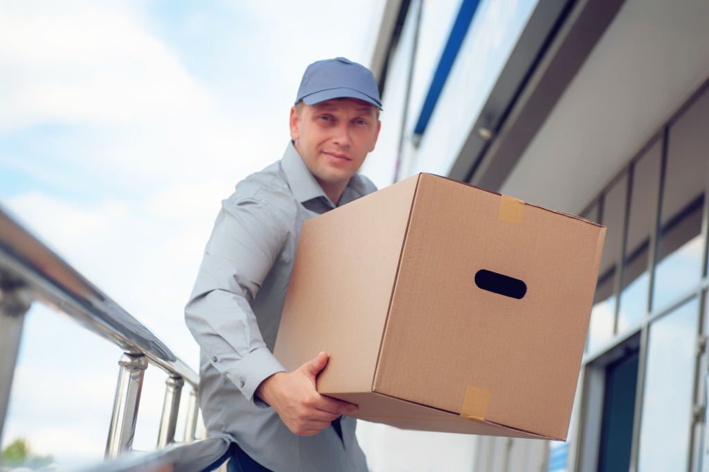 A man in a gray suit in his hands with a cardboard box against the background of the supermarket.