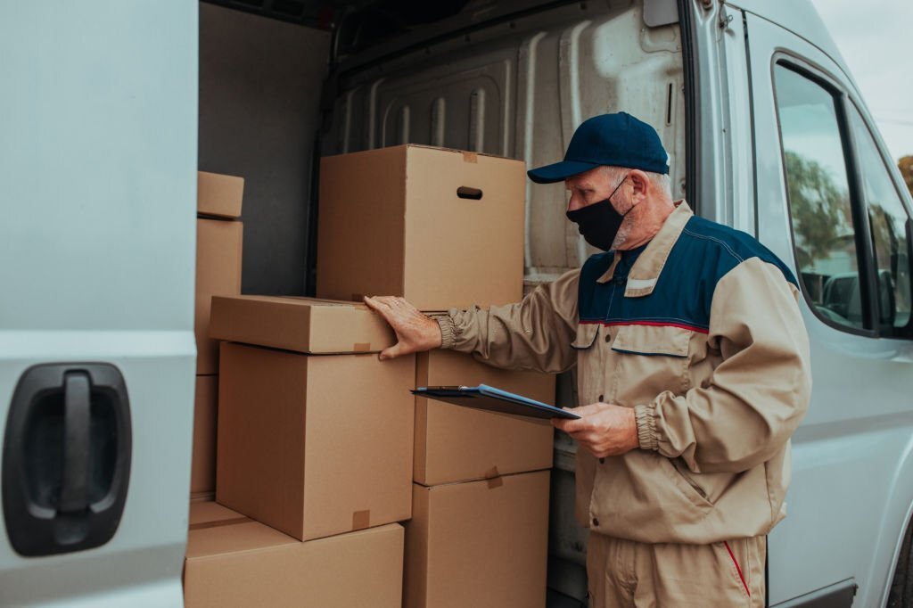 A worker carrying cardboard box while making a deliver and checking order on his list