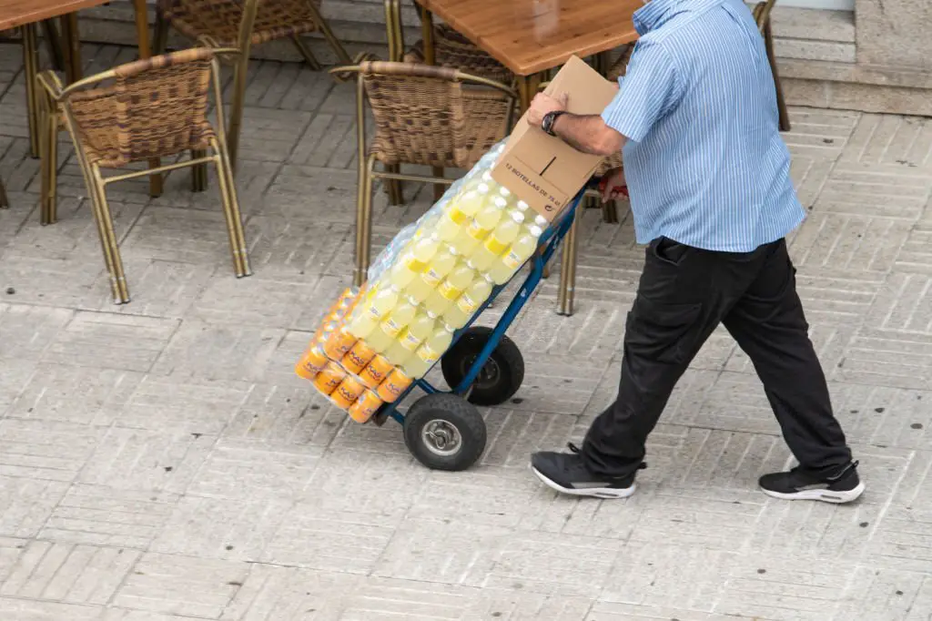 Man carrying drinks on hand cart on sidewalk