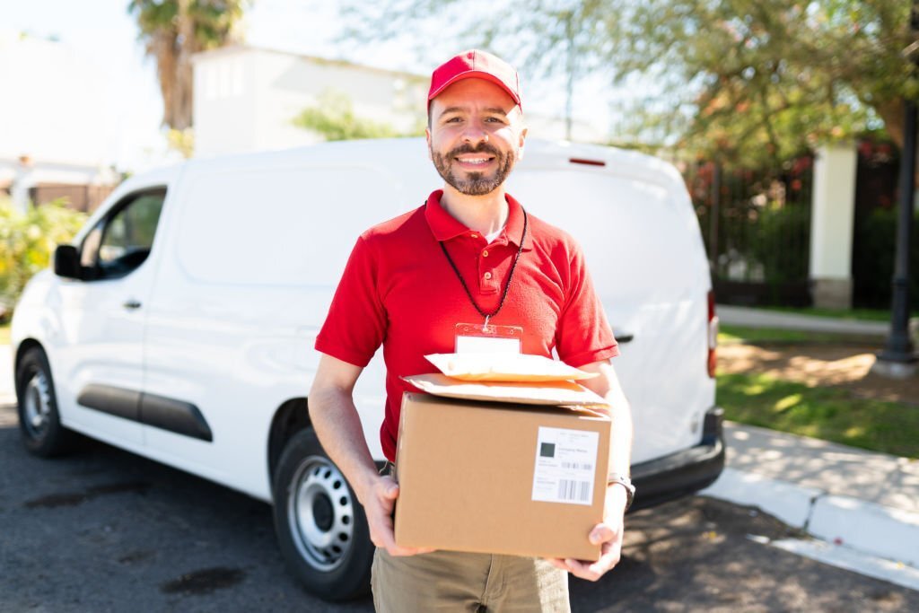 Portrait of a happy delivery courier with a white van smiling while holding some parcels and packages